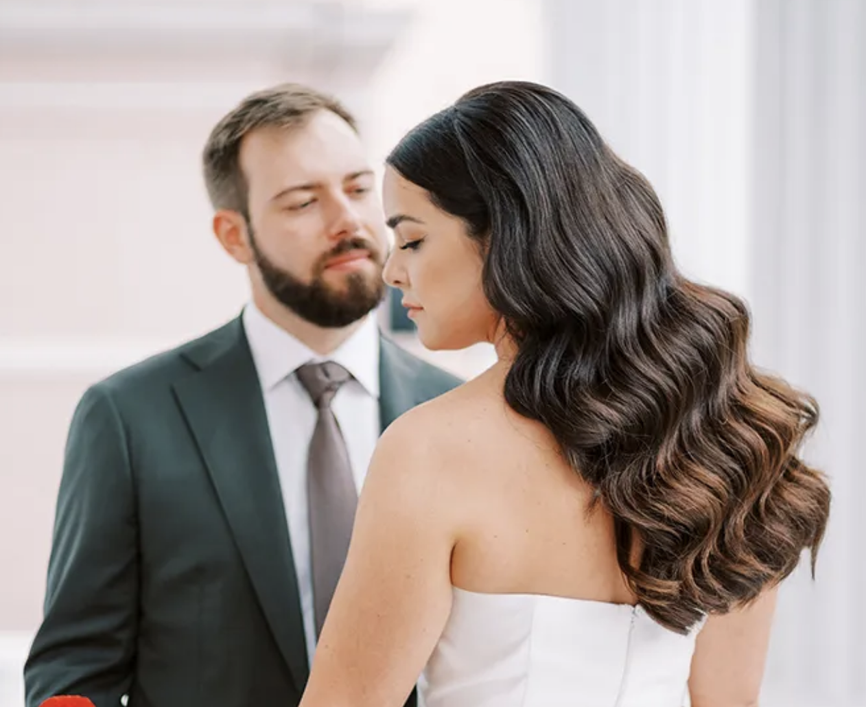 Bride with long brown curly hairstyle standing beside groom on wedding day